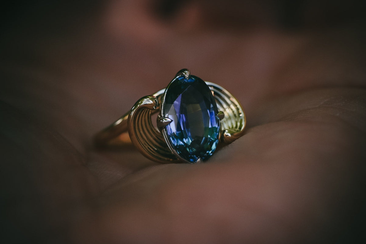 Moira Patience teal sapphire carved flowing engagement ring in hand