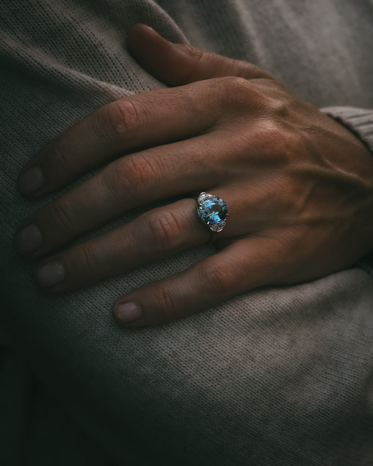 Ghlas oval teal sapphire and half-moon diamond ring in platinum, worn on the hand at an angle