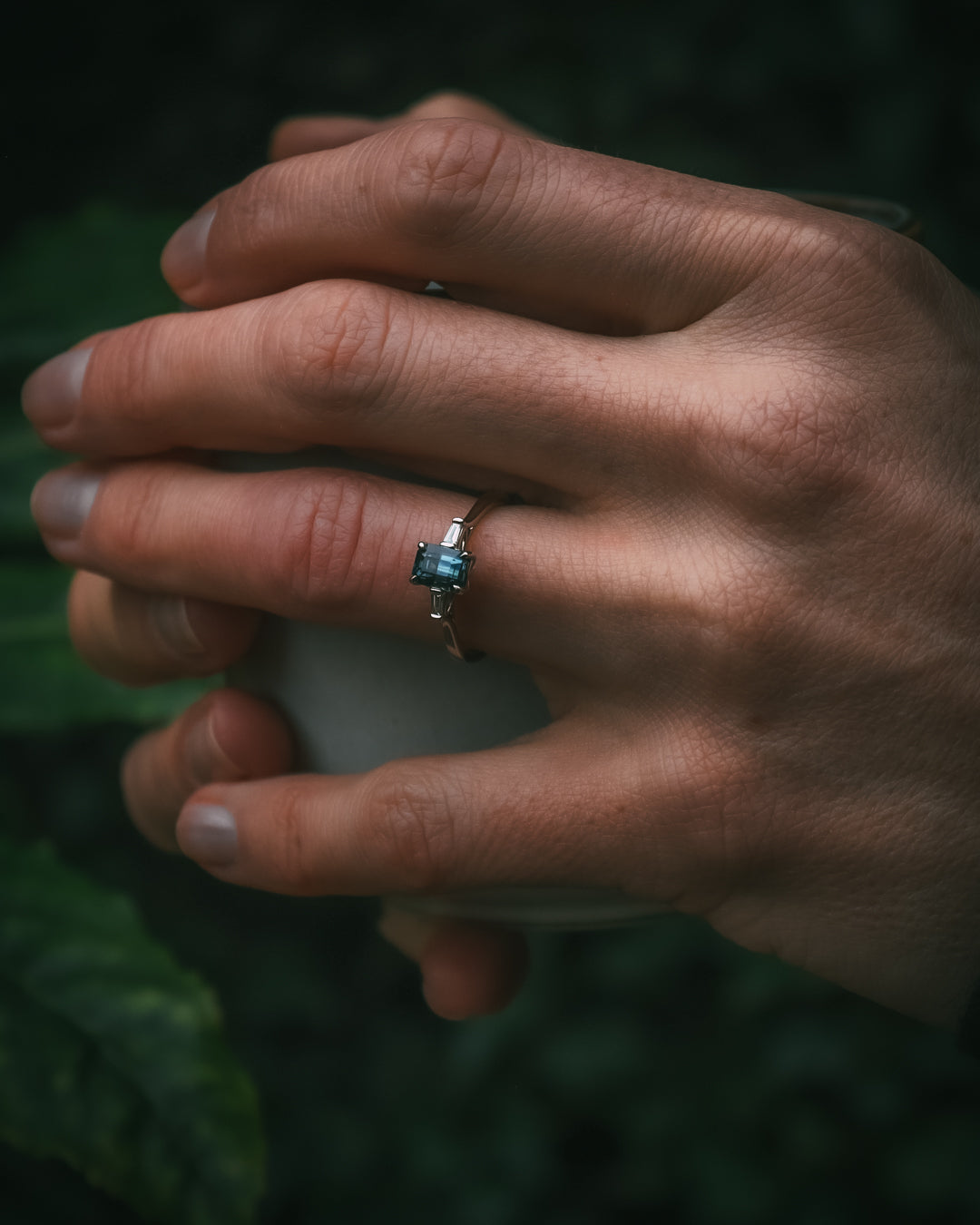 Sròn octagon step-cut teal sapphire ring holding cup