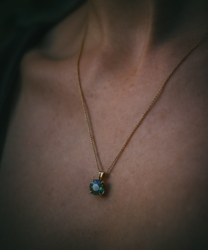 Teal sapphire Petal Pendant in 18ct yellow gold worn on the neckline, soft natural light.