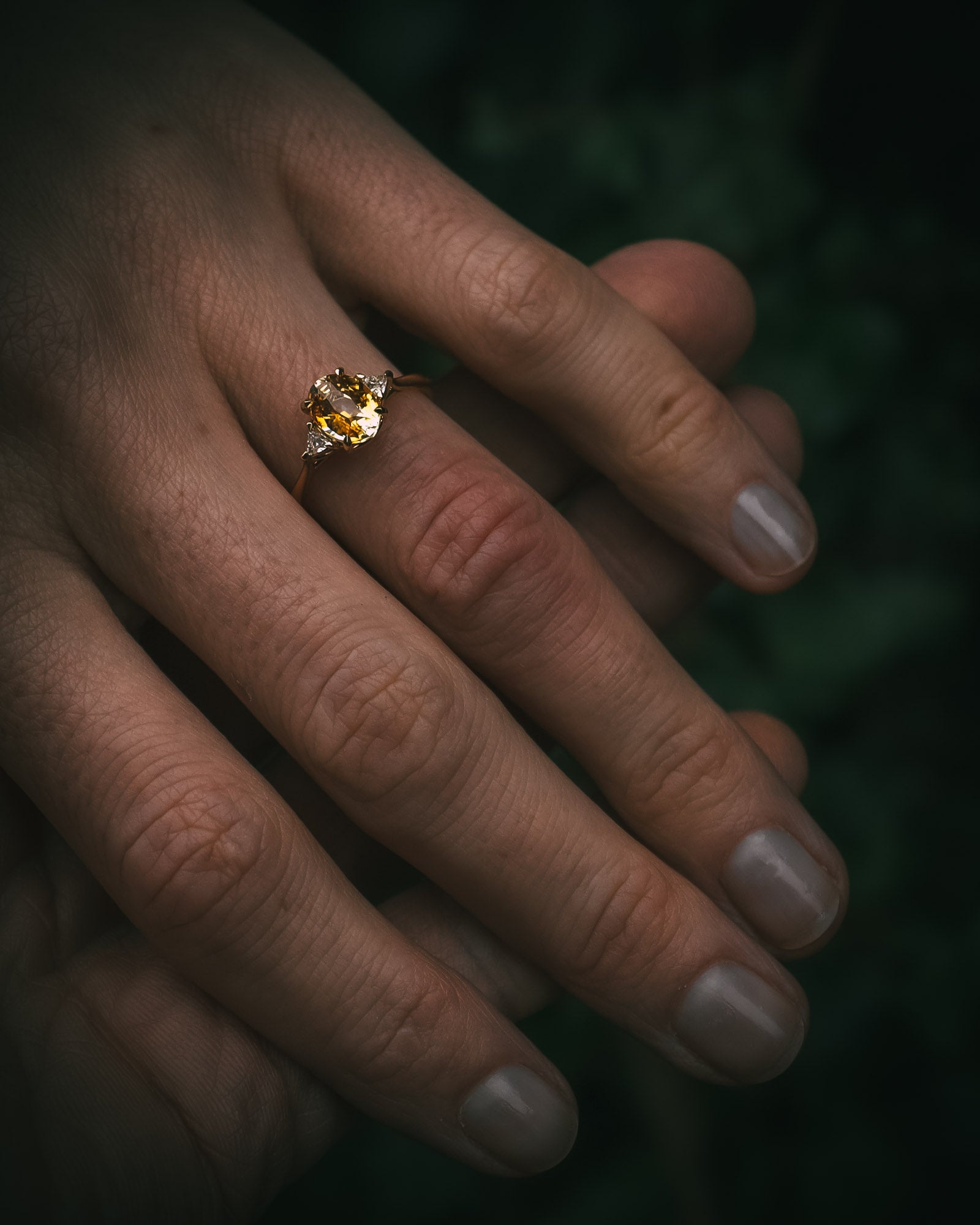 Fidra 2.04ct oval mixed-cut yellow and orange sapphire with trillion-cut diamond side stones on hand