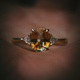 Fidra 2.04ct oval mixed-cut yellow and orange sapphire with trillion-cut diamond side stones in hand