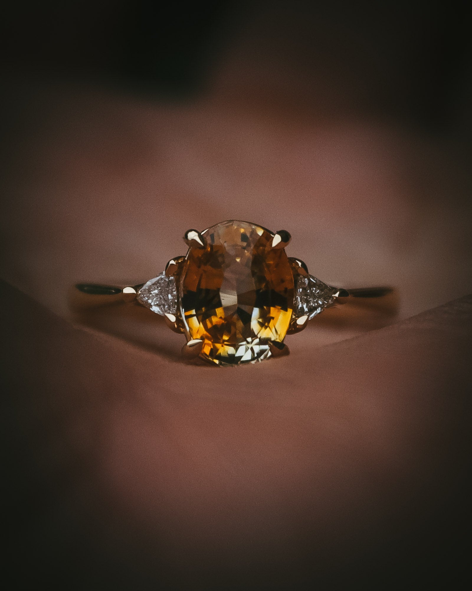Fidra 2.04ct oval mixed-cut yellow and orange sapphire with trillion-cut diamond side stones in hand